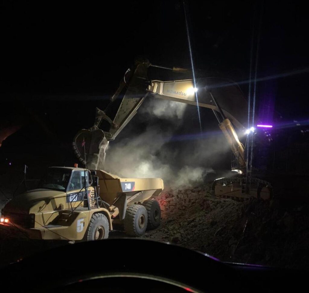 Excavadora cargando un camión articulado durante una operación nocturna.