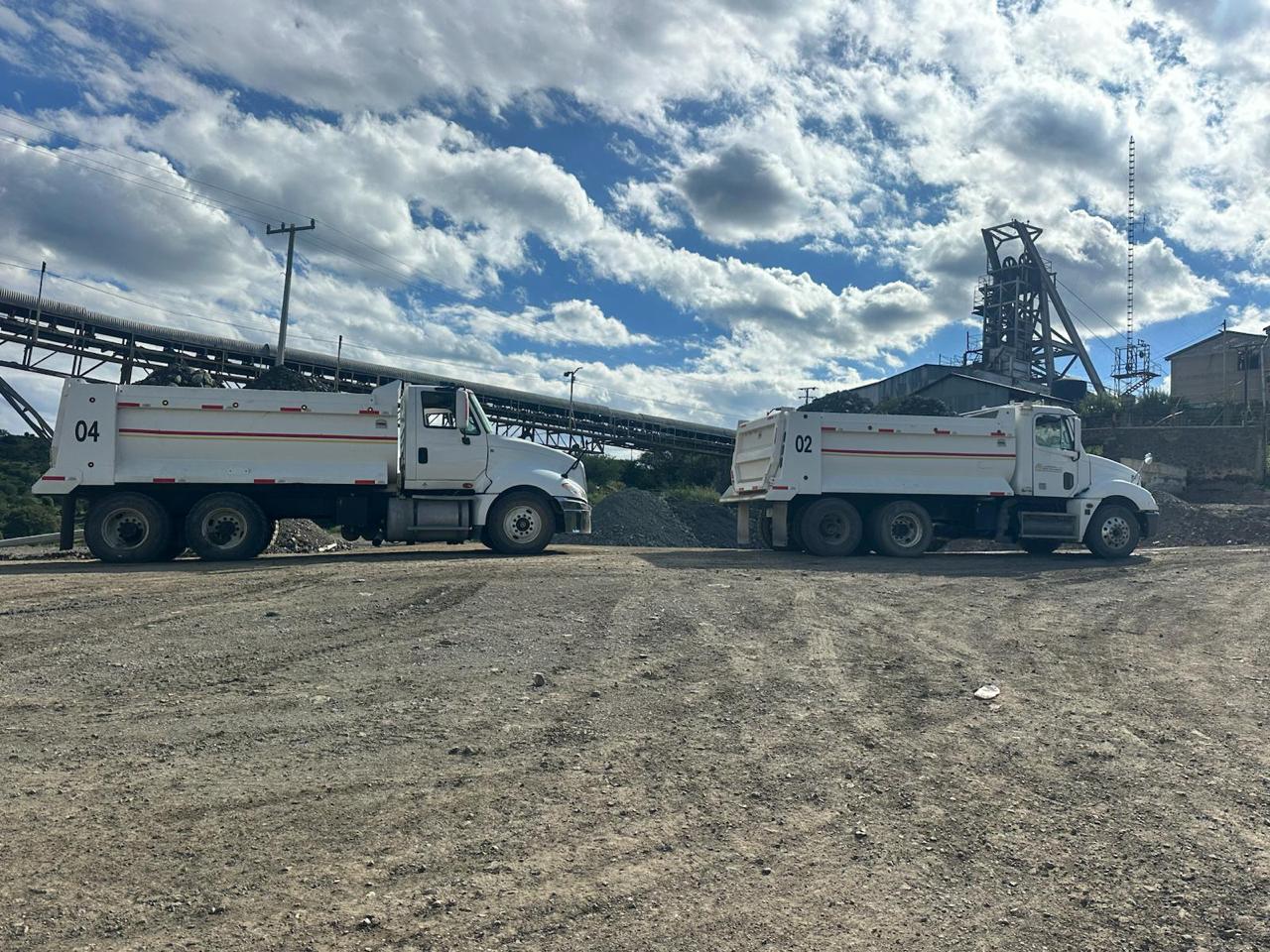 Dos camiones de volteo blancos en una instalación industrial.
